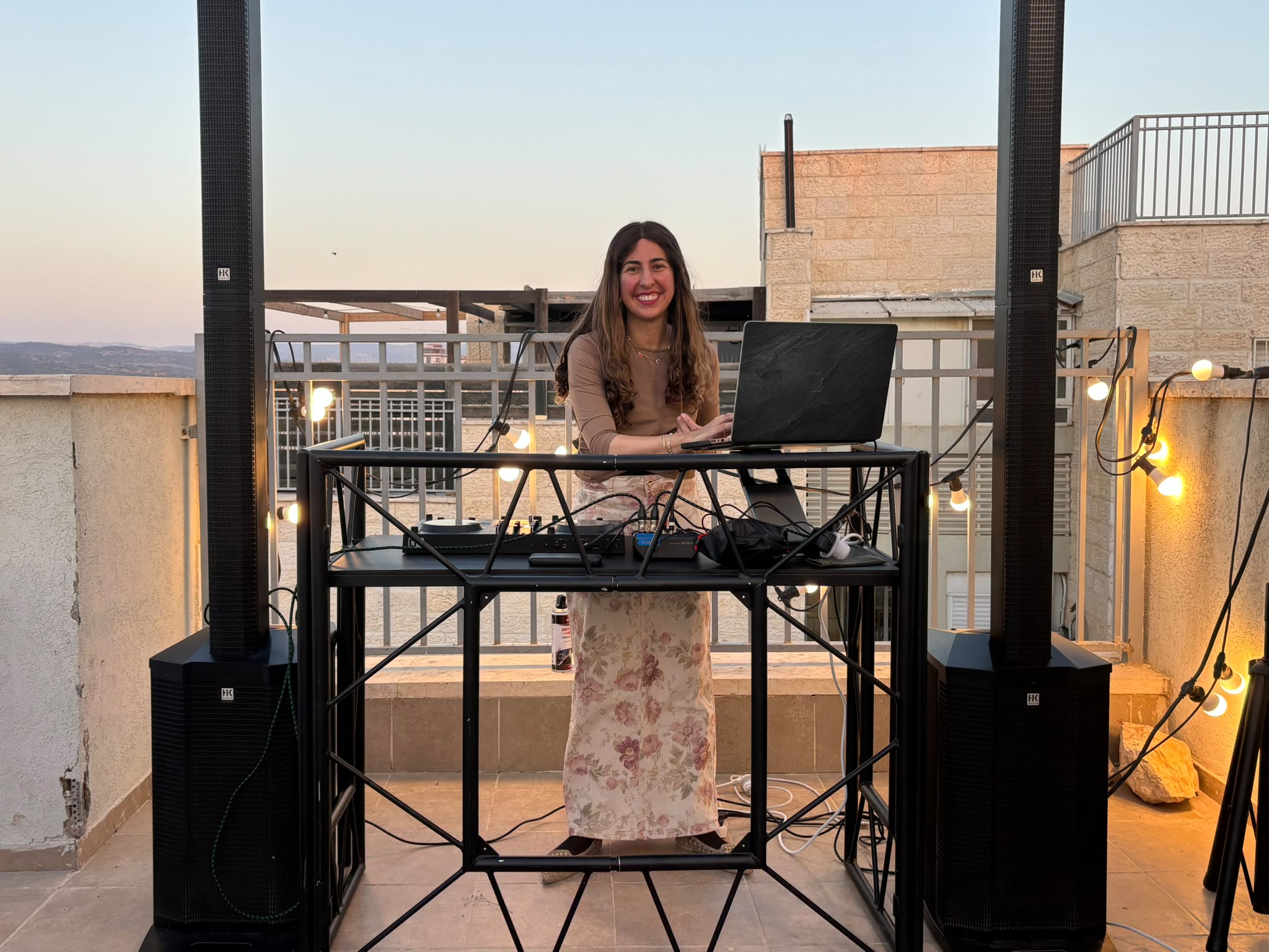 DJ Shira smiling behind her DJ setup at an outdoor event